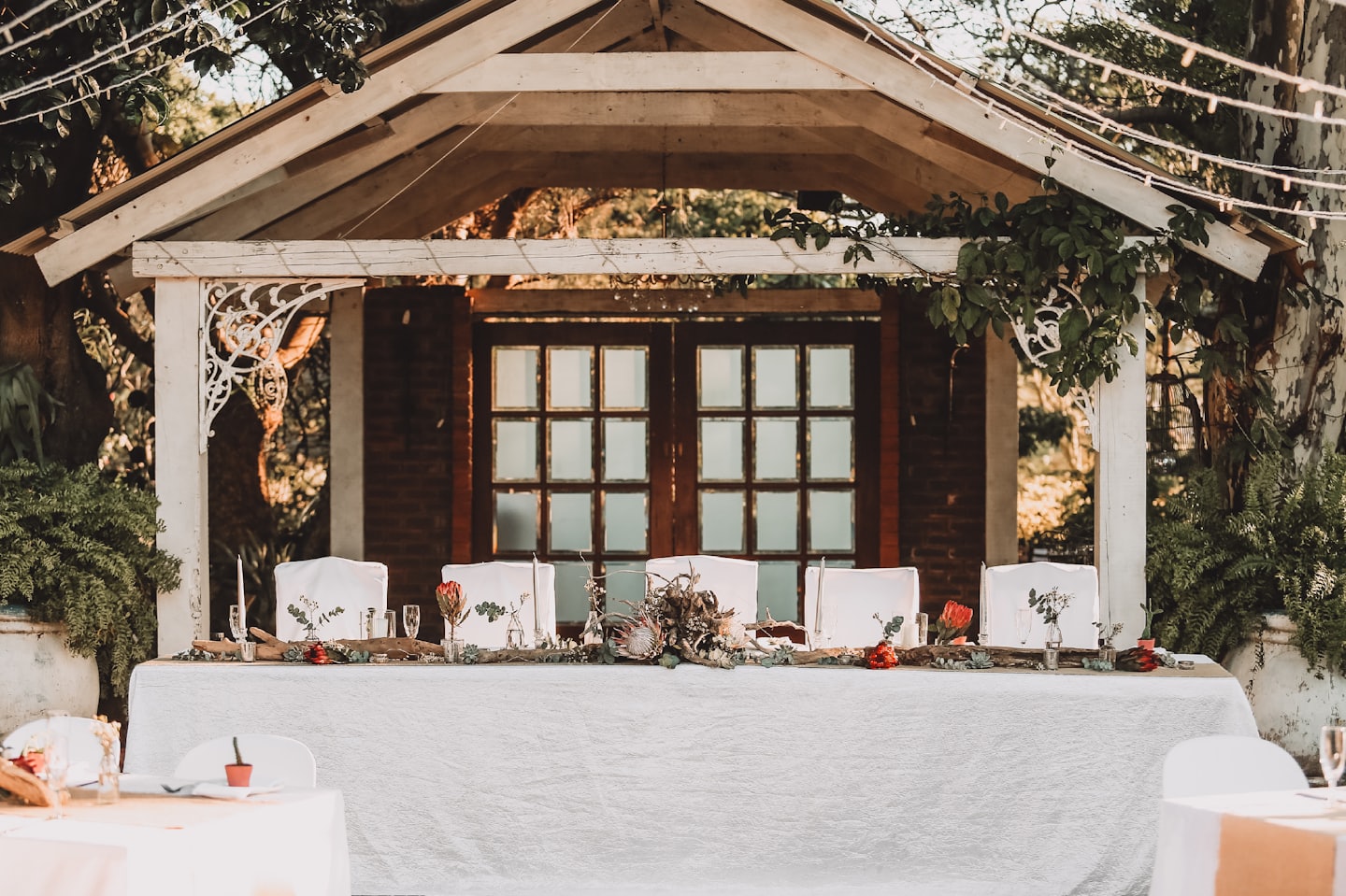 Mesa de recepción de bodas al aire libre bajo una pérgola con luces.