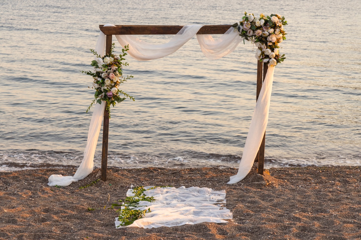 Arco de boda decorado en una playa con arreglos florales y el océano de fondo.